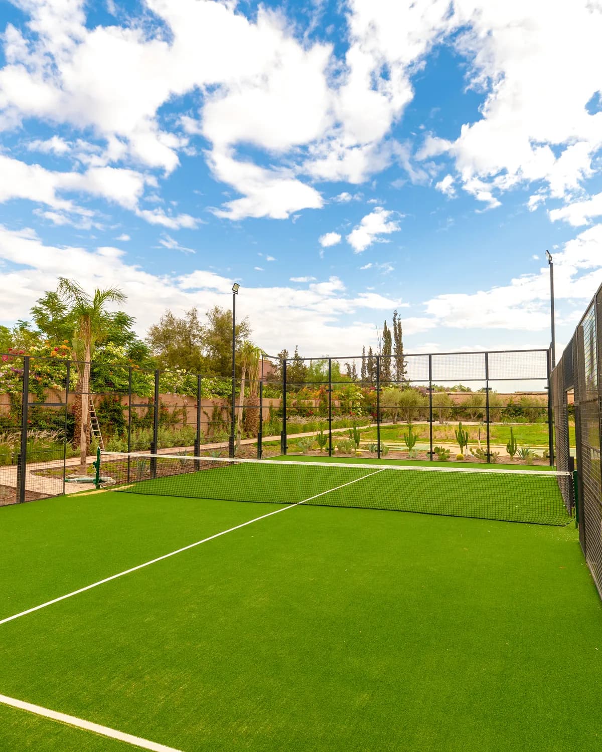 Het padelveld van de villa, met de tuin en de muur van bougainville erachter